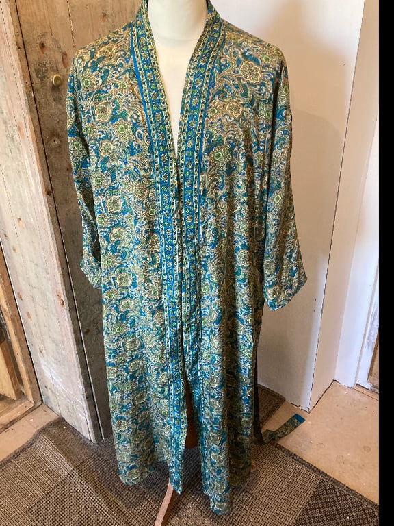 Lang kimono med blå, grønne og beige mønstre, vist på en mannequin i et rum med trævægge og måtter på gulvet. (2)