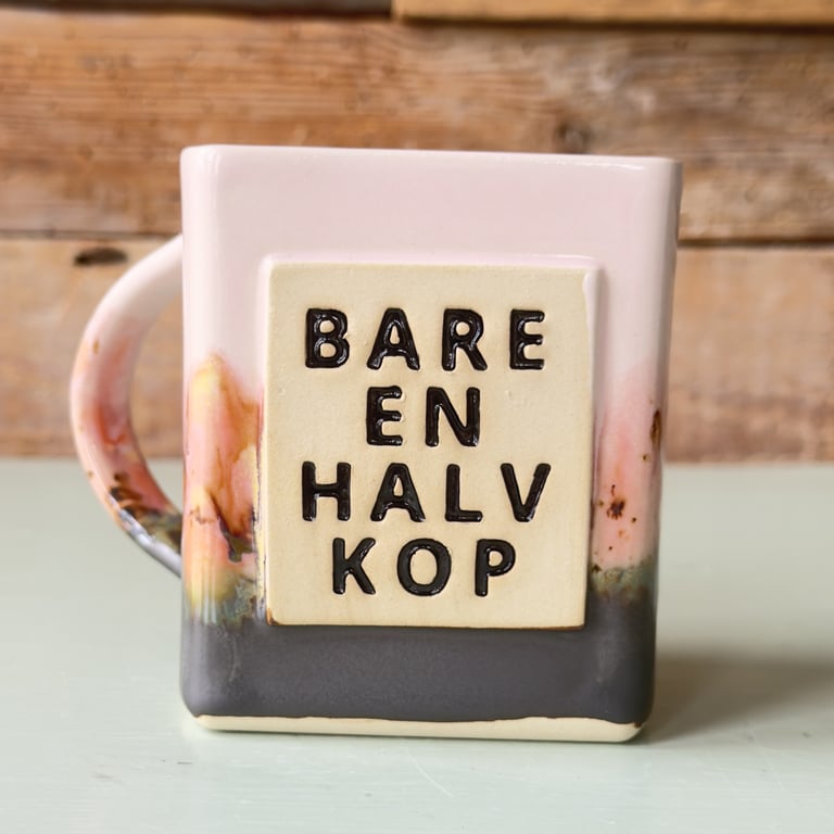 Hvid og grå keramikkop med tekst "Bare en halv kop" på forsiden.