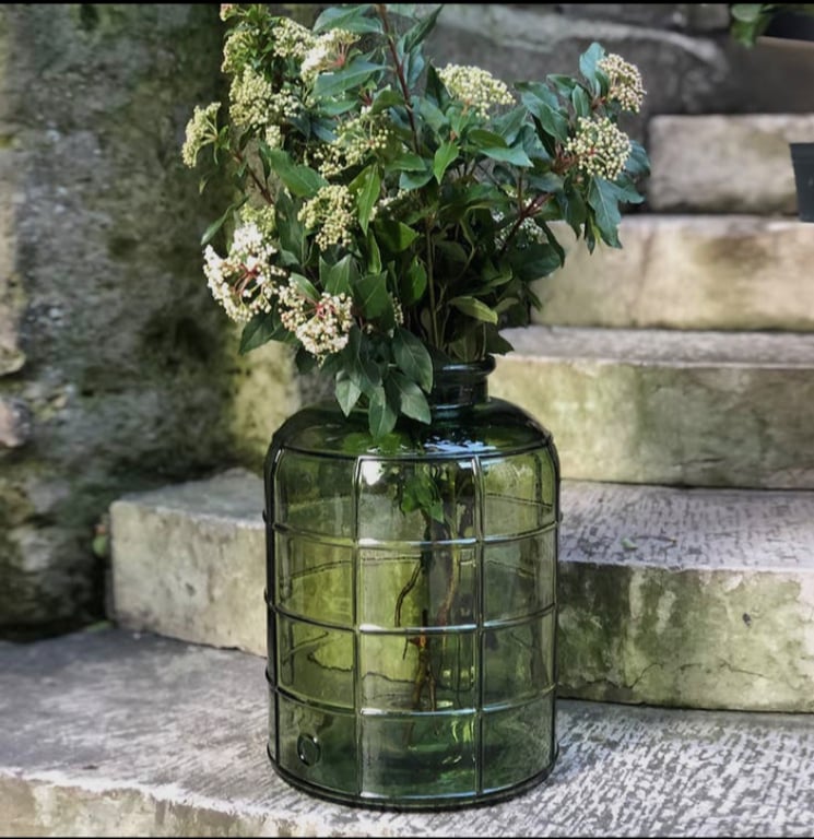 Grøn glaskrukke med blomster og grønne blade placeret på stentrin udendørs. (2)