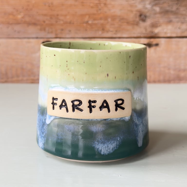 Keramikkrus med grønne, blå og beige nuancer med teksten "FARFAR" i sort.