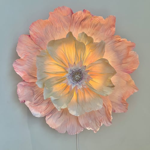 Stor væglampe formet som en blomsterblomst med sarte, lyserøde og gule kronblade, der lyser op indefra. (1)