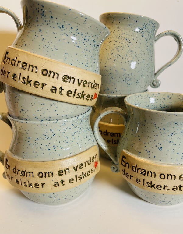 Blåspraglede keramikkrus med hank og beige mærke med dansk tekst "En drøm om en verden der elsker at elskes" og lille rød hjerte.