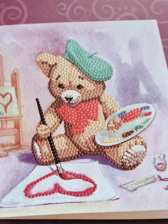 Bamse med grøn malerhat og rød butterfly maler et hjerte med rød maling på et stykke papir.