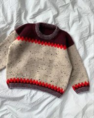 Strikket sweater i beige med røde og mørkerøde mønstre, lagt ud på en hvid seng. (1)