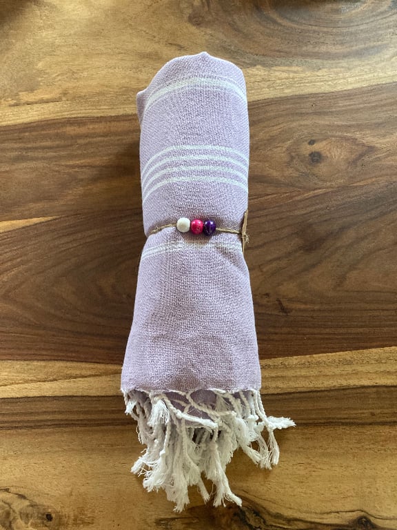 Lilla klud med hvide striber, rullet sammen og bundet med snor med farverige perler, lagt på træbord. (2)