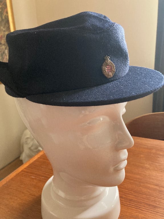 Sort kasket med metalemblem på fronten, placeret på en hvid mannequin hoved. (2)