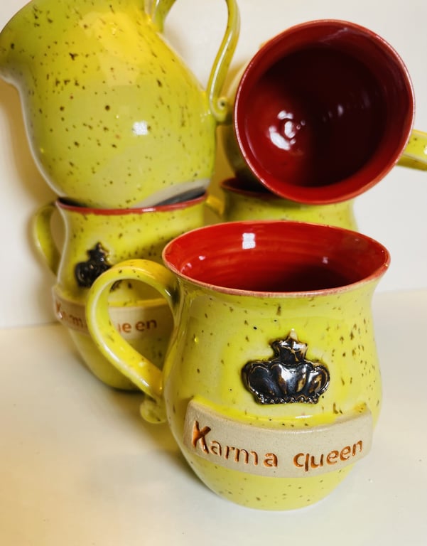 Fire guldfarvede keramikkrus med rød inderside, hvoraf det forreste har teksten "Karma queen" og en sort krone dekoration.