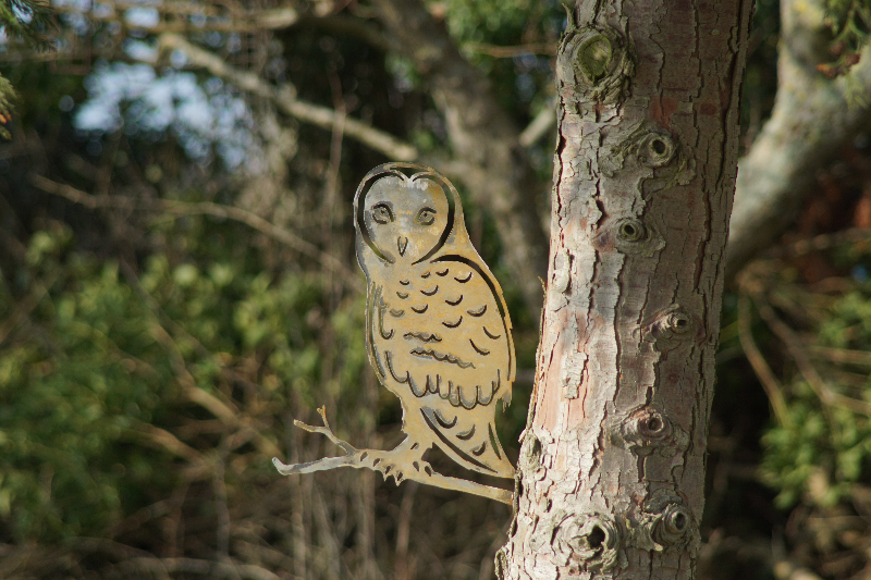 Metalfugl formet som en ugle monteret på en træstamme i en skov.