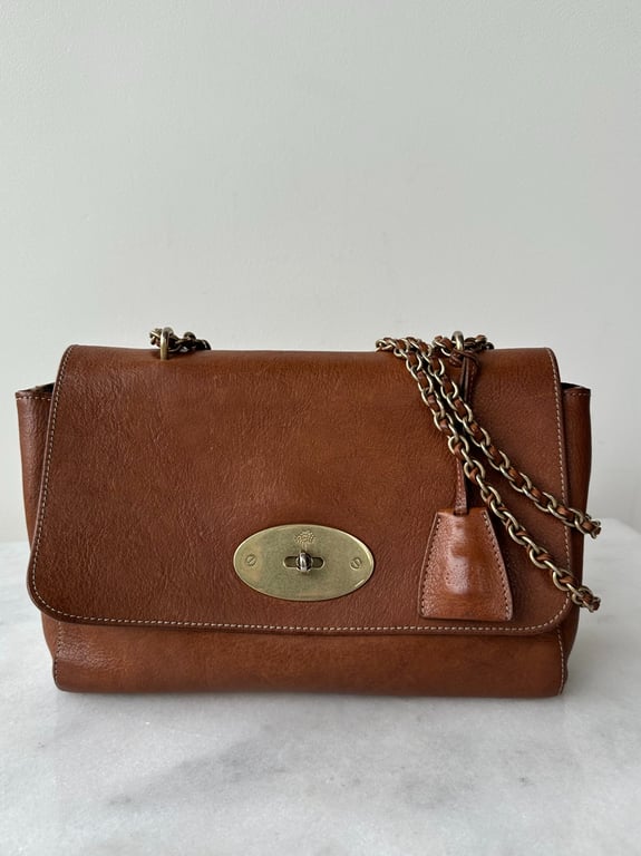 Brun lædertaske med kæderem og oval guldfarvet lukning foran.