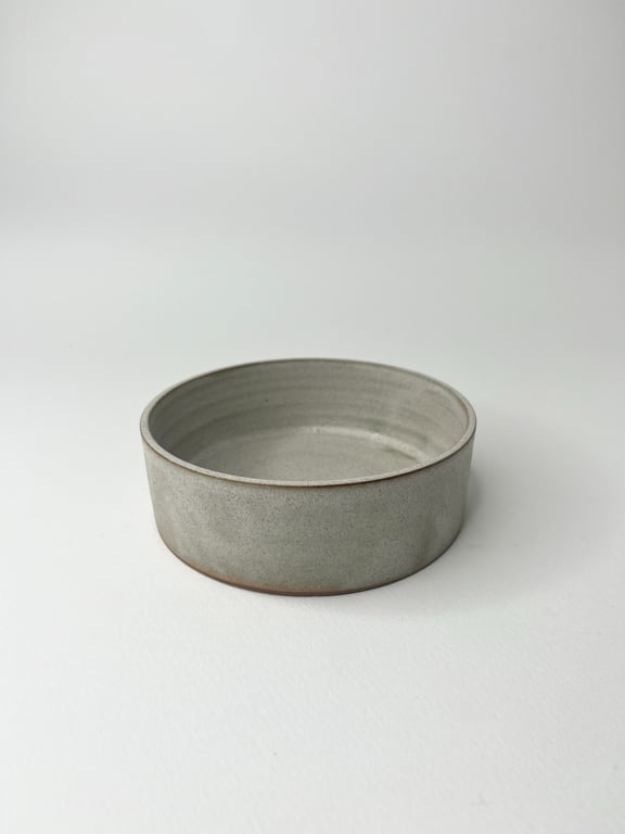 Grå keramisk skål med lav højde og glat overflade placeret på hvid baggrund.