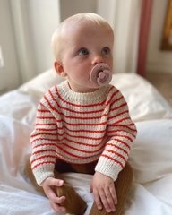 Baby med sut i munden iført en stribet rød og hvid sweater, siddende på en hvid seng. (4)
