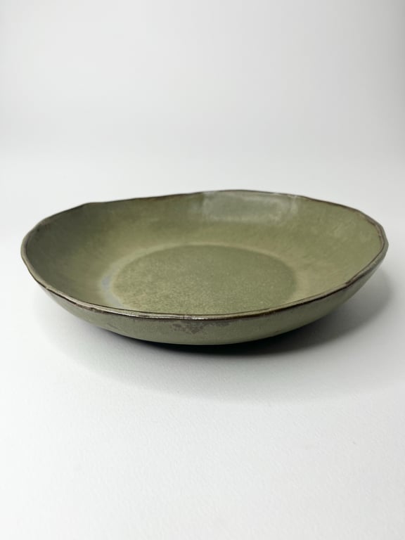 Grøn keramisk tallerken med let ujævn kant på hvid baggrund.
