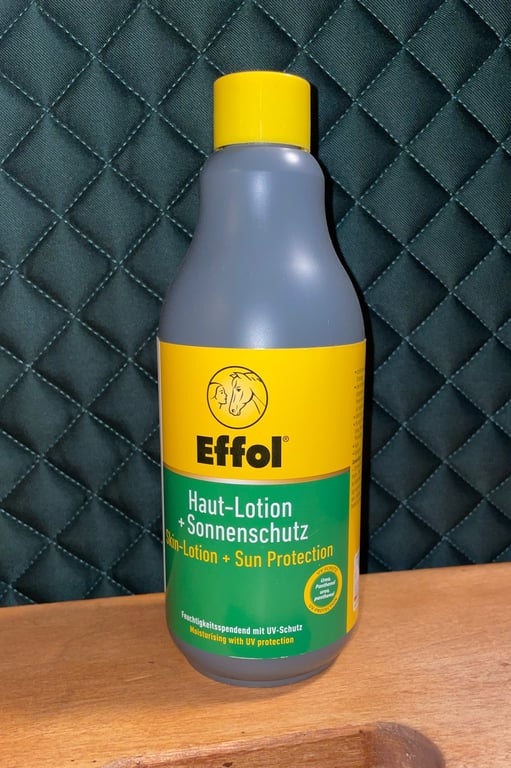 Flaske med Effol hudlotion og solbeskyttelse til heste, placeret på et bord foran en mørk, quiltet baggrund.