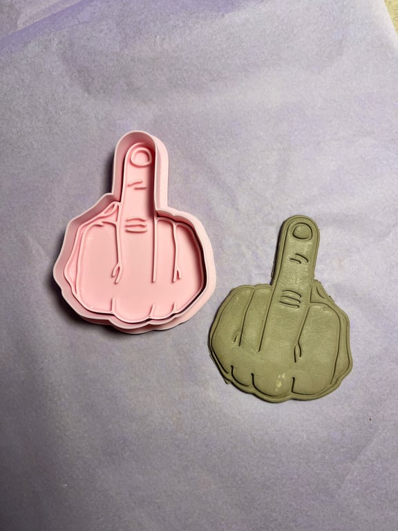 To udstikkere til småkager formet som en hånd, der viser langefingeren, en i lyserød plastik og en i grå.