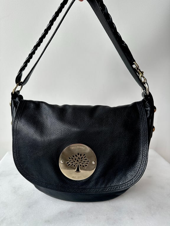 Sort skuldertaske i læder med rund messingplade og trælogo foran.