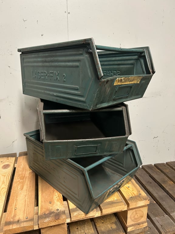 Tre stablede metal opbevaringskasser mærket "LAGER-FIX 2" på en træpalle mod en hvid væg.