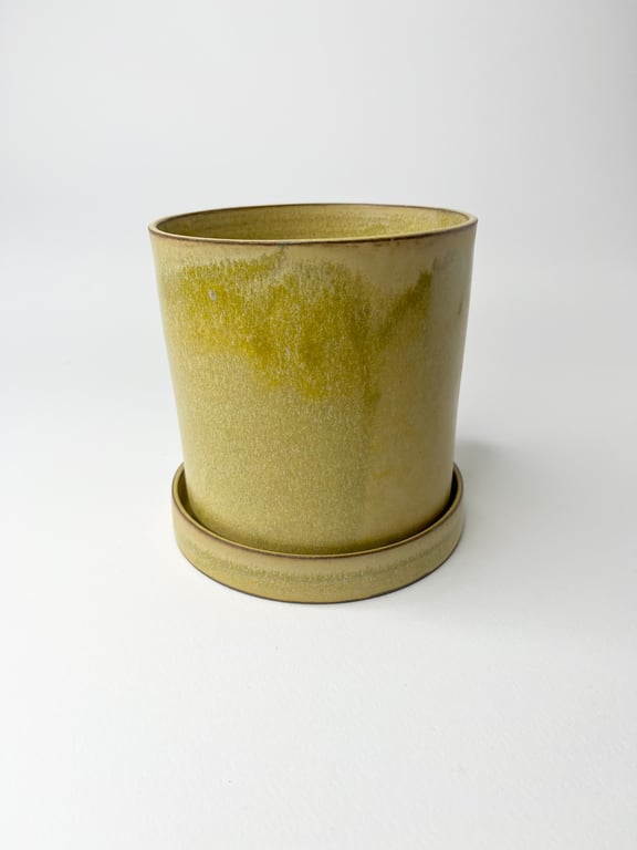 Grøn keramisk blomsterpotte med tilhørende vandopsamler på hvid baggrund.