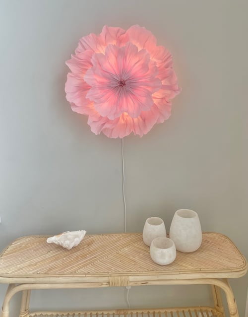 Væglampe formet som en stor pink blomst, hængende over et flettet rattan-bord med tre hvide keramikkrukker og et stort hvidt muslingeskal. (1)