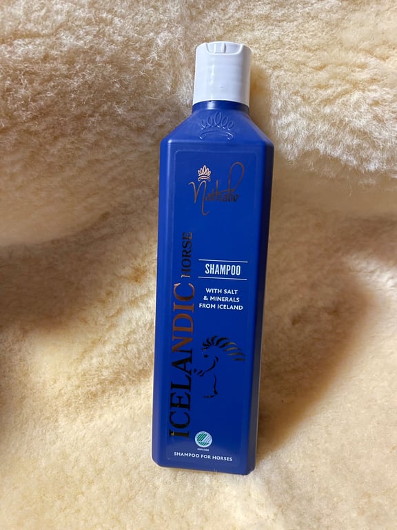 Flaske med blå shampoo til islandsheste, placeret på lyst, blødt stof.