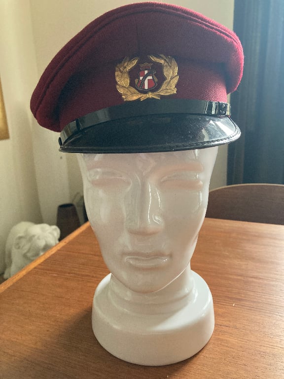 Buste i hvid keramik iført en rød uniformskasket med sort skygge og gulddetalje foran, placeret på et træbord indendørs. (2)