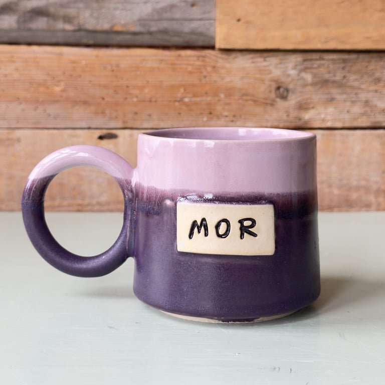 Lilla keramikkrus med påskriften "MOR" foran mod en træbaggrund.