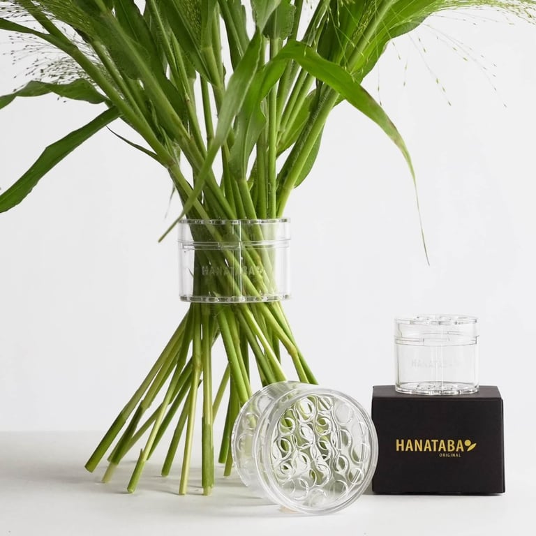 Clear plastic blomsterholder sat omkring stilkene på en buket samt to ekstra blomsterholdere ved siden af en sort æske med teksten "HANATABA".