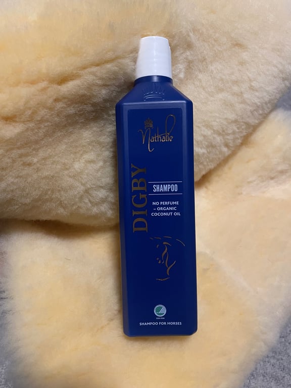 Blå flaske med Nathalie Digby shampoo til heste liggende på lysegul blød uld eller lammeskind.