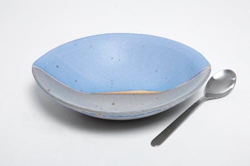 Blå og grå keramisk dyb tallerken med ske på hvid baggrund.