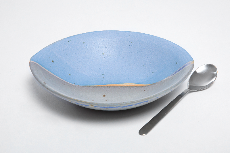 Blå og grå keramisk dyb tallerken med ske på hvid baggrund.