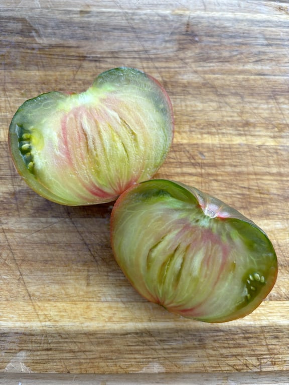 To skiveskårne heirloom tomater med grønne og lyserøde nuancer på en træskærebræt.