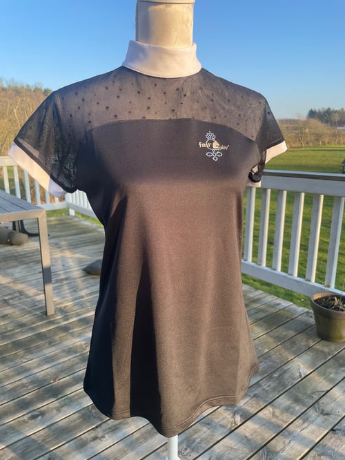 Sort og hvid kortærmet sportsbluse med mesh og prikmønster øverst, med "fair play" logo på forsiden, vist på en mannequin uden hoved, stående på en træterrasse udendørs. (1)