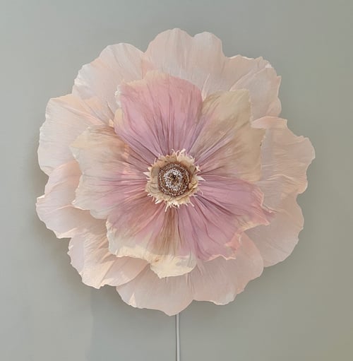 Stor kunstig blomst i sarte nuancer af lyserød og beige, monteret på en grå væg. (1)