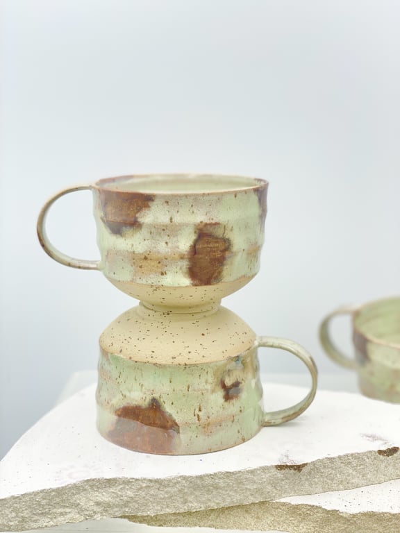 To krus i keramisk materiale med grønne og brune pletter, stablet oven på hinanden.