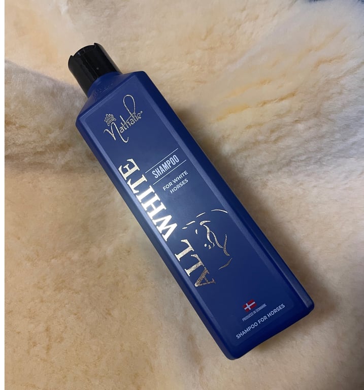 Flaske med blå shampoo til hvide heste, mærket "All White Shampoo" fra Nathalia, placeret på en lys pels.