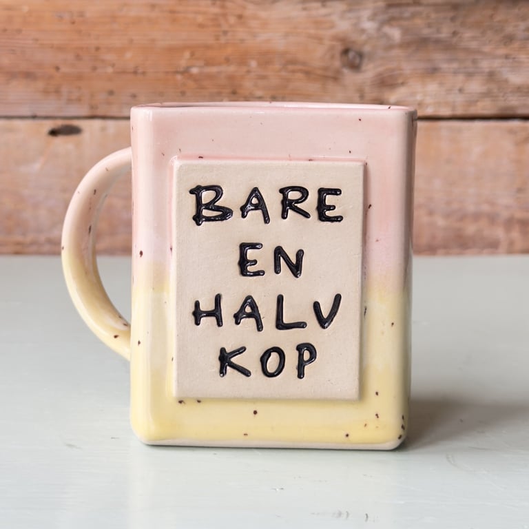 Kræmmerhusformet kop i pastelfarver med teksten "Bare en halv kop" på forsiden.