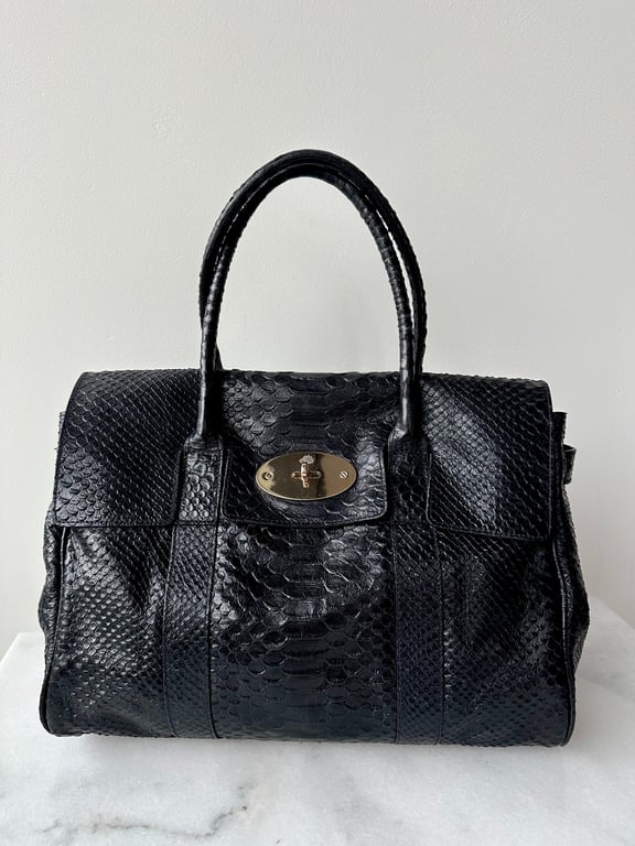 Sort håndtaske i slangeskindslook med rundet hank og metalspænde foran.