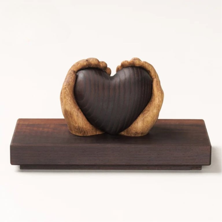 Træskulptur af to hænder, der holder et hjerte, placeret på en rektangulær træplade.