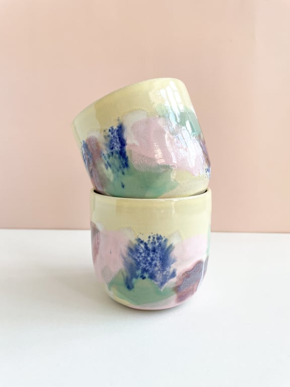To små keramik krus med pastel farvede abstrakte mønstre, stablet mod en beige baggrund.