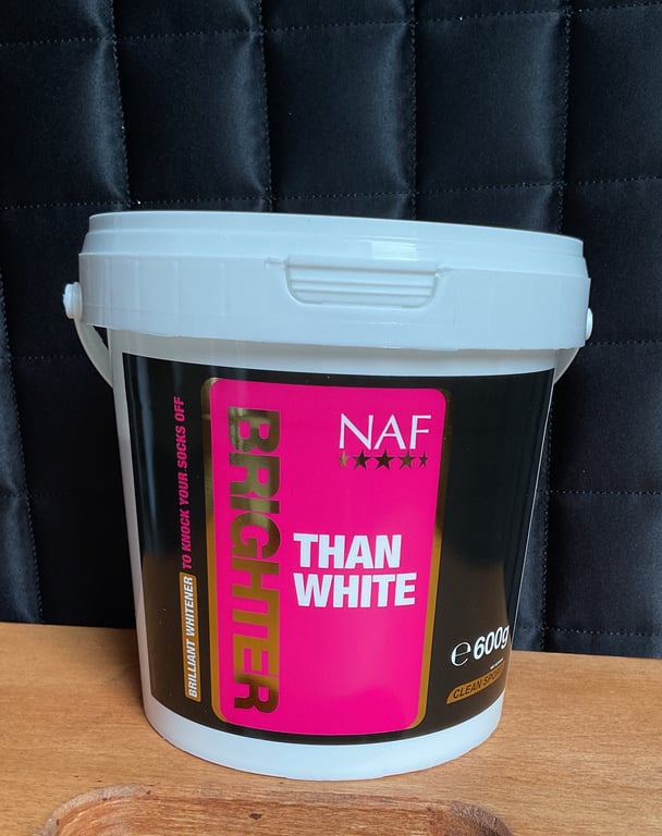 Bøtte med NAF Brighten Than White hvidgøringsmiddel på træbord med sort baggrund.