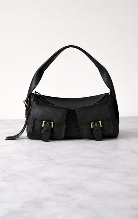 Sort skuldertaske i læder med to forlommer og guldspænder, placeret på marmoroverflade.