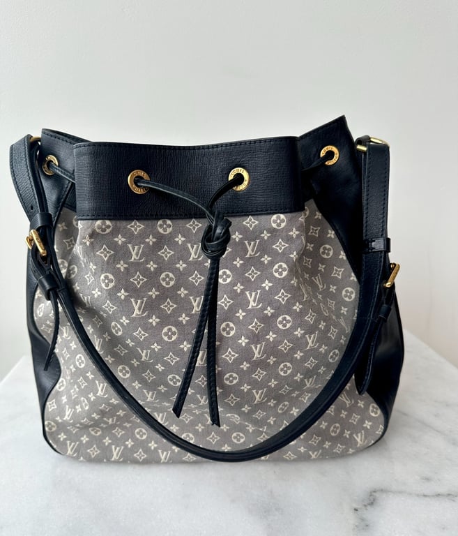 Sort og grå Louis Vuitton skuldertaske med monogrammønster og gulddetaljer på hvid marmorbordplade.