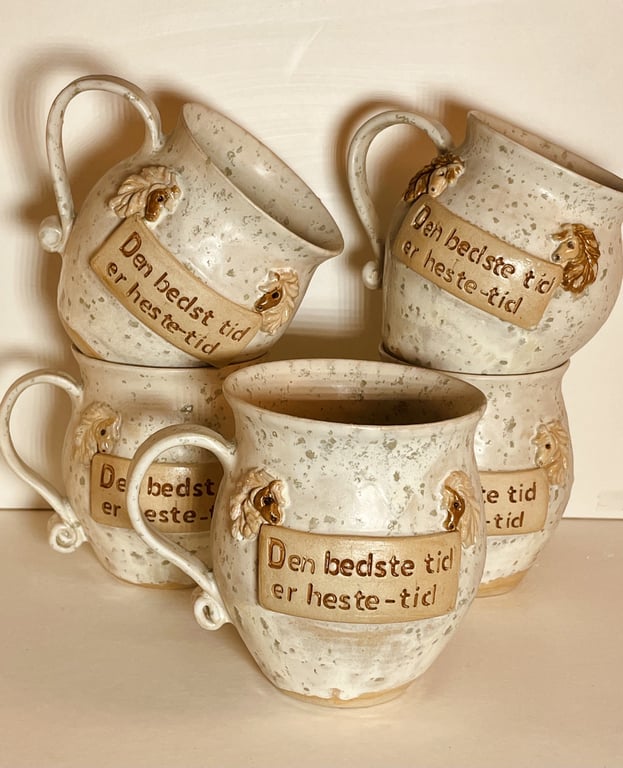Fem keramik krus med håndtag og hesteudsmykning, hver med teksten "Den bedste tid er heste-tid" på dansk.