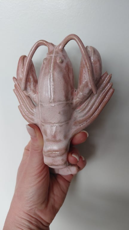 Hånd, der holder en rosa keramisk skulptur formet som en hummer.