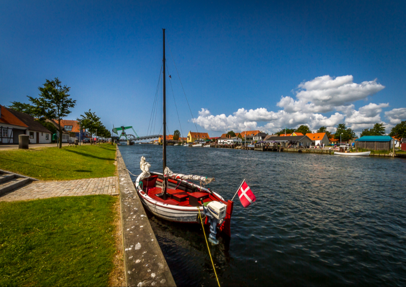 En lille sejlbåd ligger til kaj i kanalen på Enø en smuk sommerdag