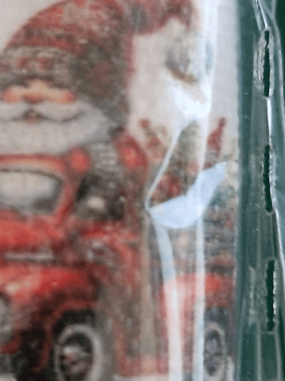 Sløret billede af en julemand i rød dragt og hue, muligt som del af julepynt eller dekoration bag glas eller plast.