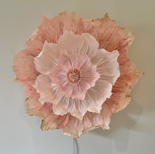 Stor, detaljeorienteret vægdekoration formet som en blomst med lag af rosenfarvede og beige kronblade på en lys væg. (1)