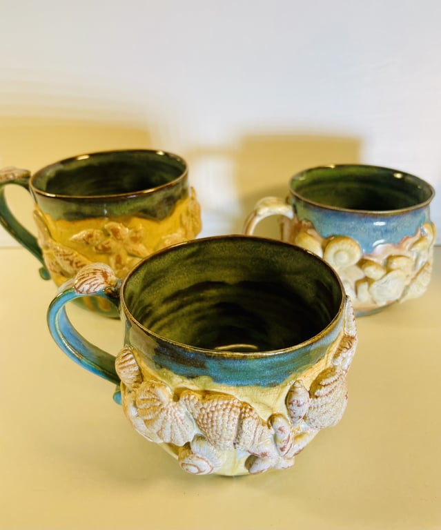 Tre keramikkrus med blå og grøn glasur, dekoreret med relieffer af havskaller.
