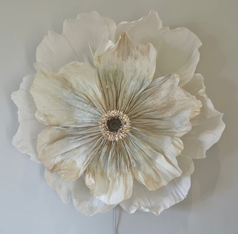 Stor, hvid blomsterdekorationslampe med teksturerede kronblade monteret på en lysegrå væg.