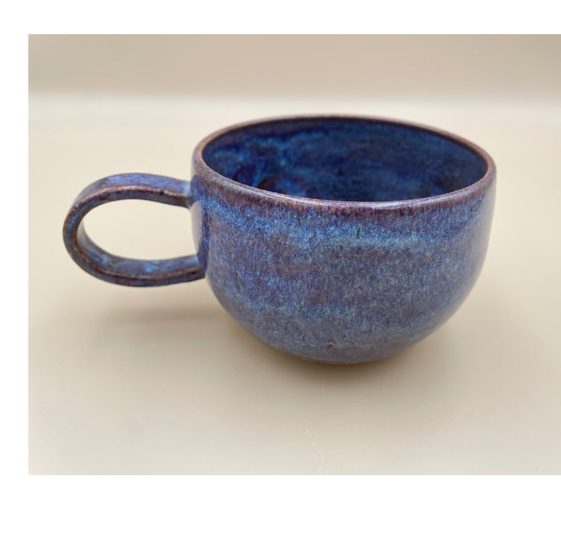 Blå keramik kaffekop med håndtag på beige baggrund.