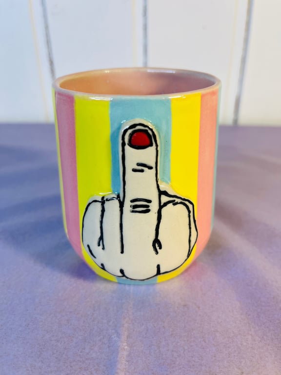 Farverig keramisk kop med horisontale striber i pink, gul og blå, dekoreret med en stor hvid hånd, der viser langemand med rød neglelak.